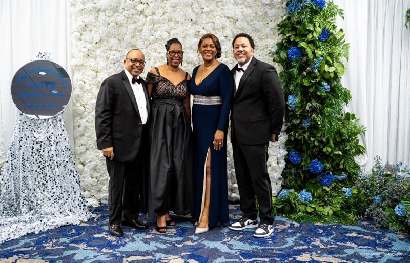 four African American adults in tuxedos and ball gowns pose for a photo at a ceremony